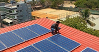 Man kneeling to install solar panels on a flat red roof in a city in Nigeria