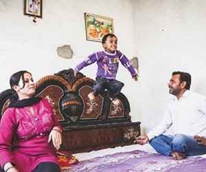 Man and woman from India sitting on a bed with their young child who is jumping