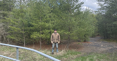 Man standing outside in front of a group of pine trees